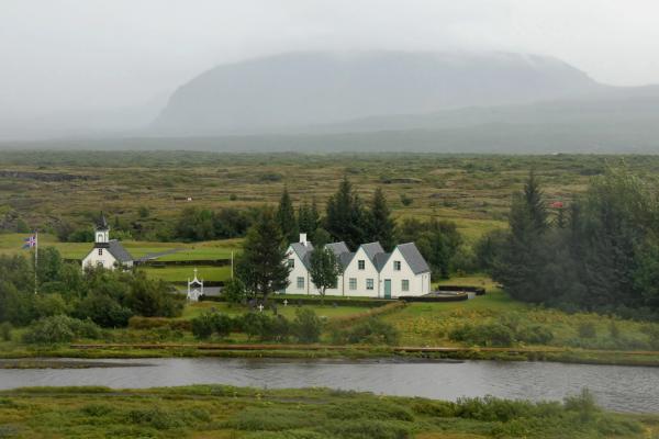 cuatro casa blancas y una iglesia junto a un río en una llanura verde