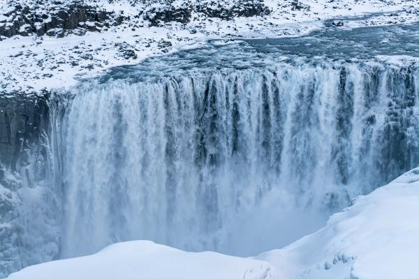 a waterfall is surrounded by snow and ice in the winter at dettifoss in iceland.