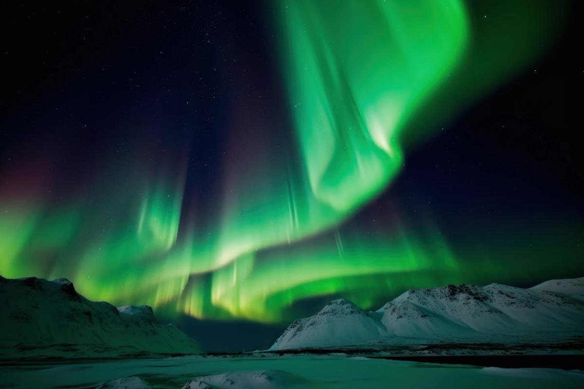 the aurora borealis is dancing in the night sky over the mountains in iceland.