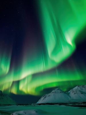 the aurora borealis is dancing in the night sky over the mountains in iceland.