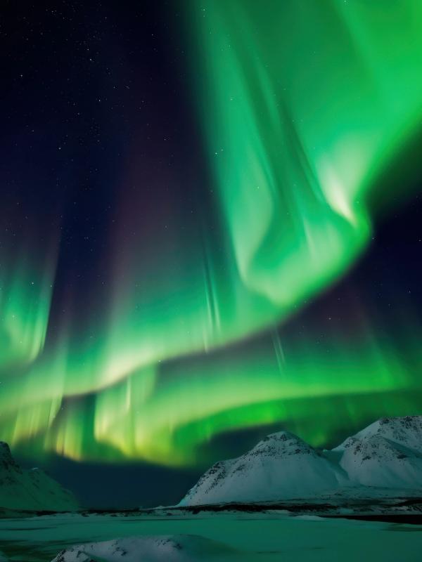 the aurora borealis is dancing in the night sky over the mountains in iceland.