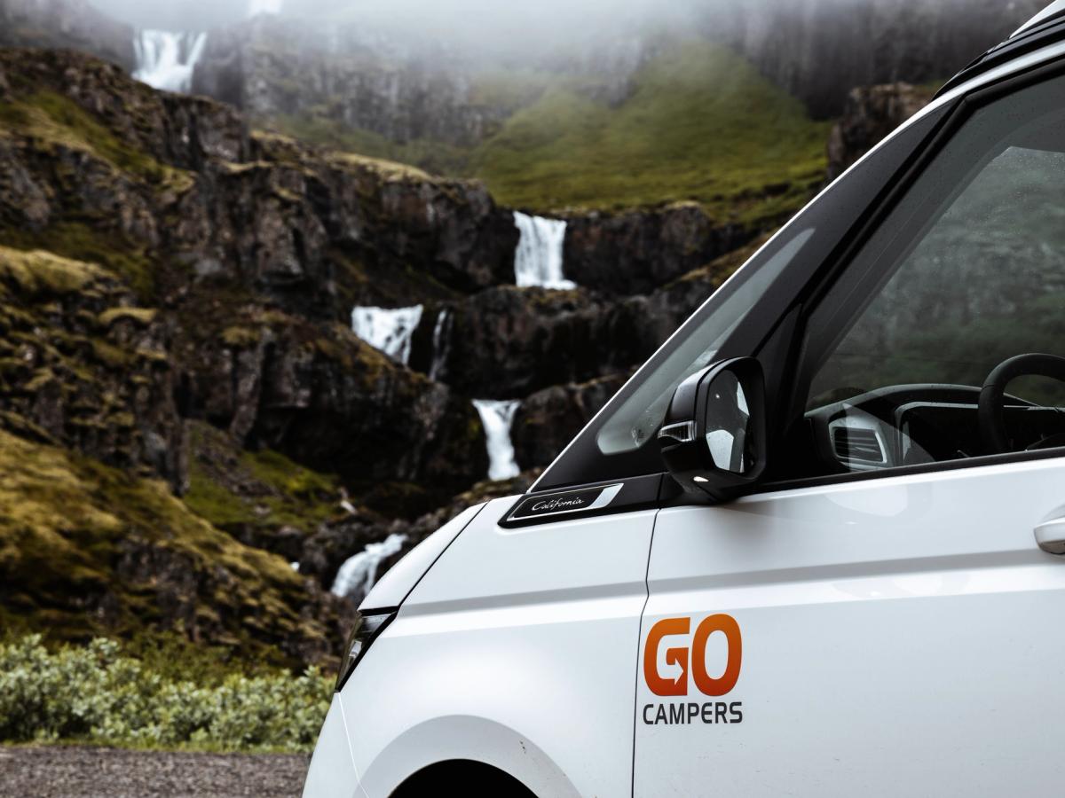 Go Campers-merki á hurð Go Campers-merkið á hvítum framdyrum með þrepaskiptan foss í bakgrunni