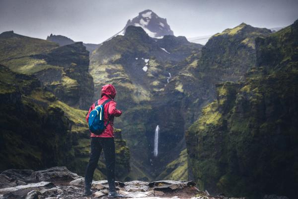 a person with a backpack is standing on top of a mountain looking at a waterfall .