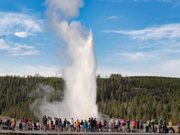 a group of people are standing on a bridge watching a geyser erupting .