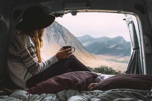 a woman is sitting in the back of a van holding a cup of coffee .