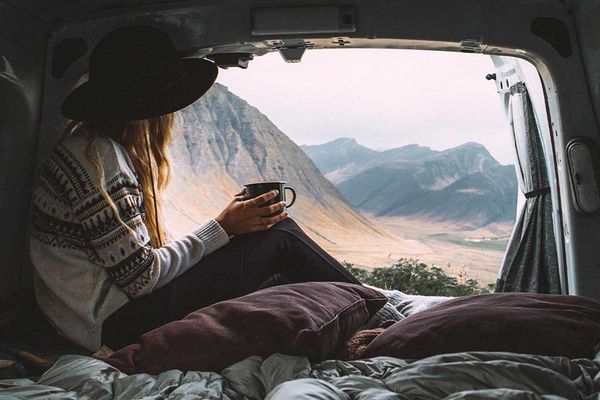 a woman is sitting in the back of a van holding a cup of coffee in iceland.