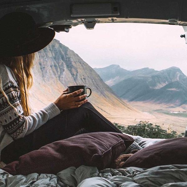 une femme est assise à l'arrière d'un fourgon et tient une tasse de café en regardant le paysage
