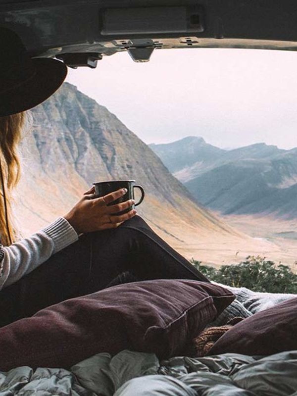 a woman is sitting in the back of a van holding a cup of coffee .