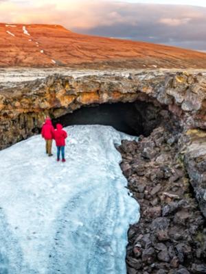 a couple of people standing on top of a snow covered cave at surtshellir in the silver circle in iceland.