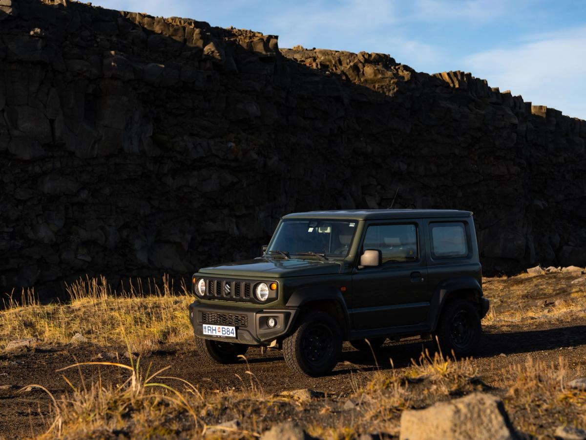 Jimny-Schotterpiste Suzuki Jimny 4x4 Mietwagen mit Schaltgetriebe in Island, geparkt auf einem unbefestigten Weg unterhalb einer dunklen Felswand