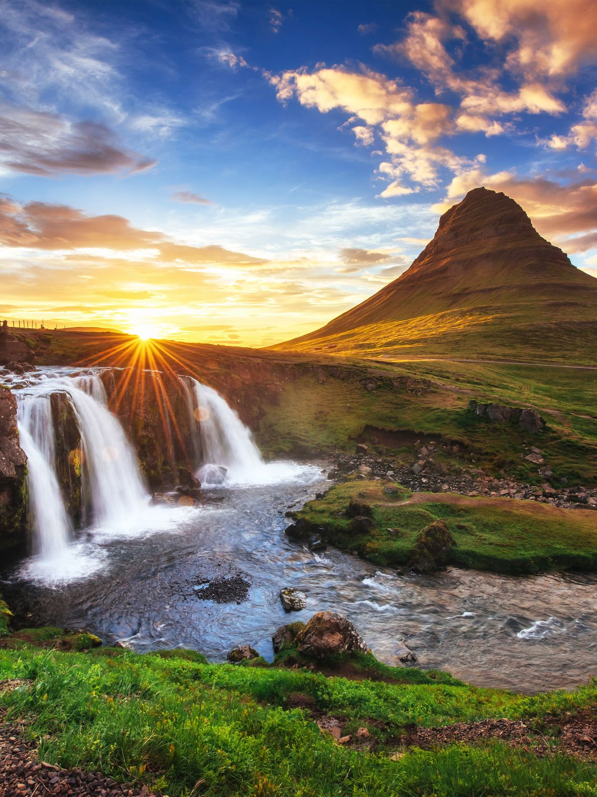 a waterfall with a mountain in the background at sunset at Kirkjufell in snæfellsnes in Iceland.