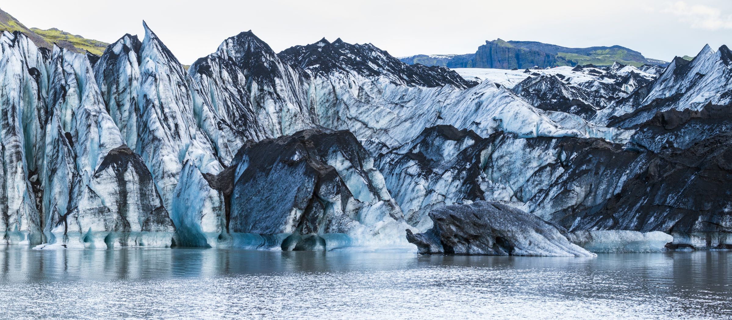 a large iceberg is melting into a lake with mountains in the background .