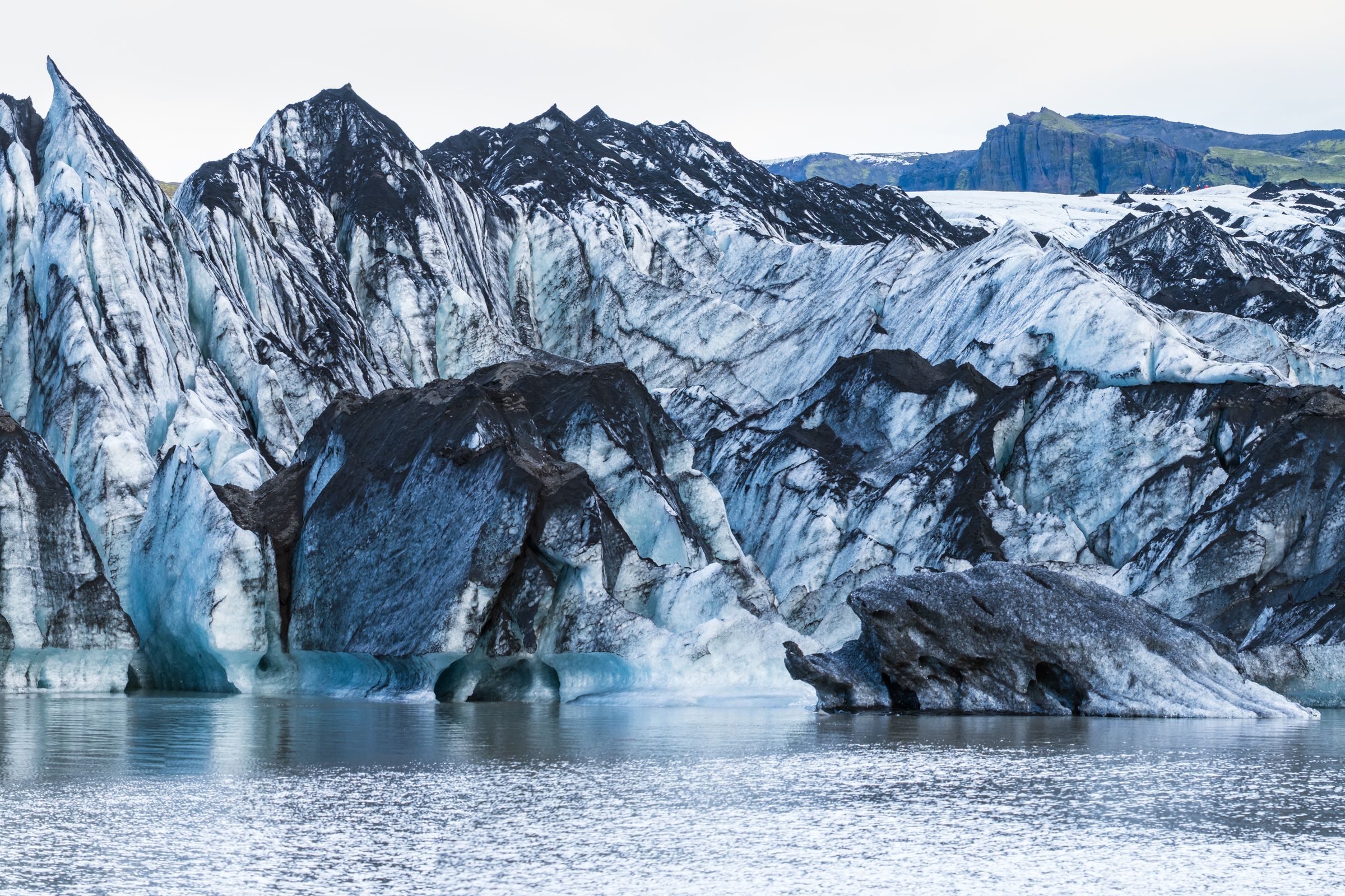 a large iceberg is melting into a lake with mountains in the background .