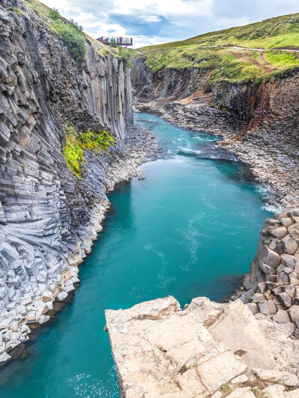 A vibrant turquoise river flows through a canyon with dark, vertical basalt column walls.