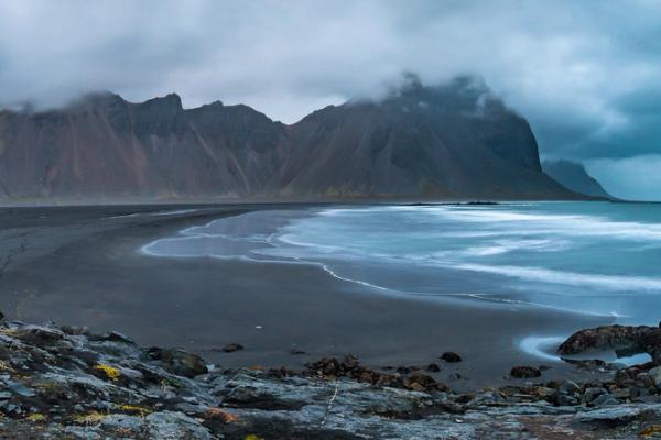 a panoramic view of a black sandy beach with mountains in the background .