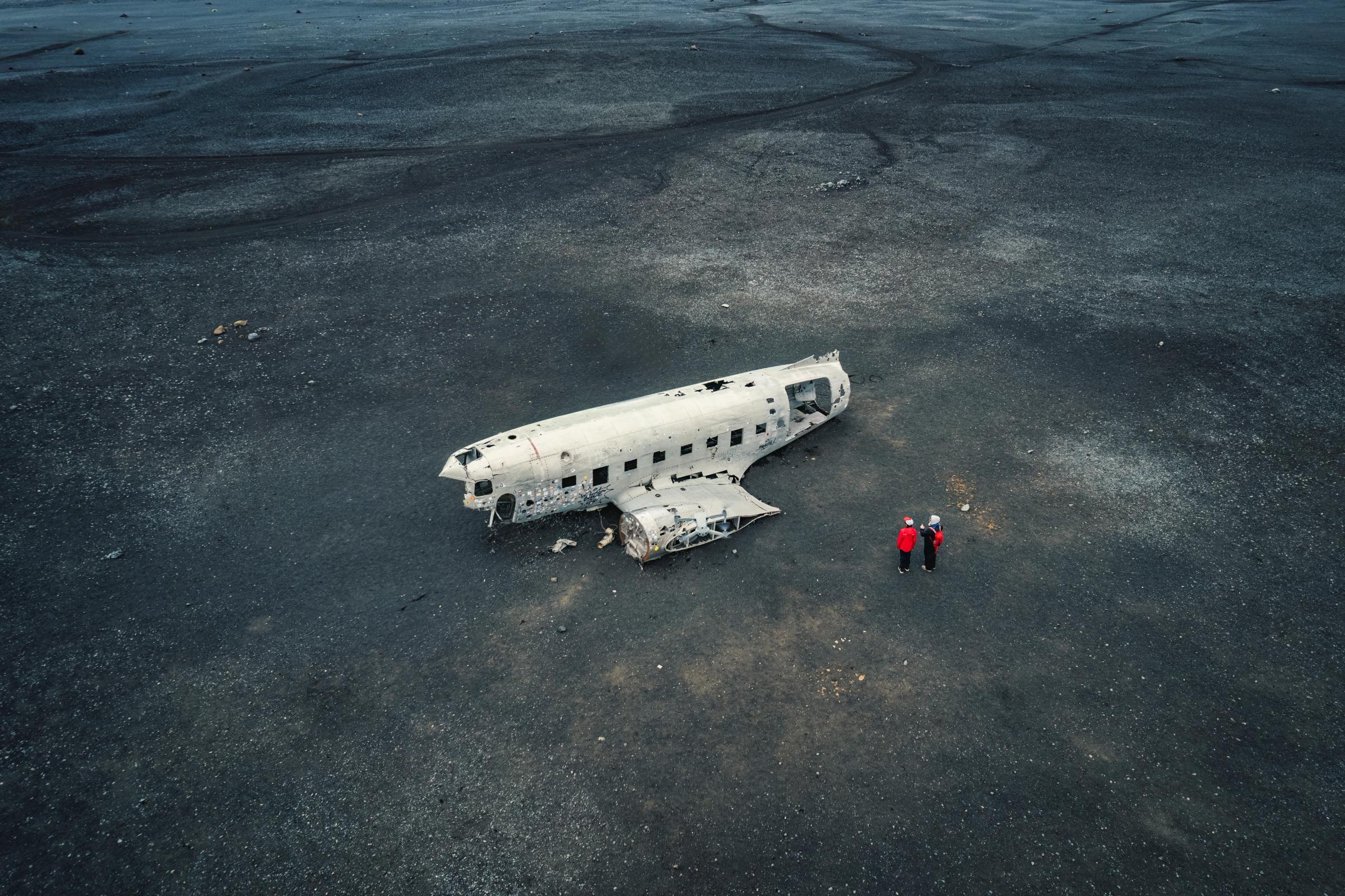 una vista aérea de dos personas de pie junto a un avión estrellado en medio de un desierto.