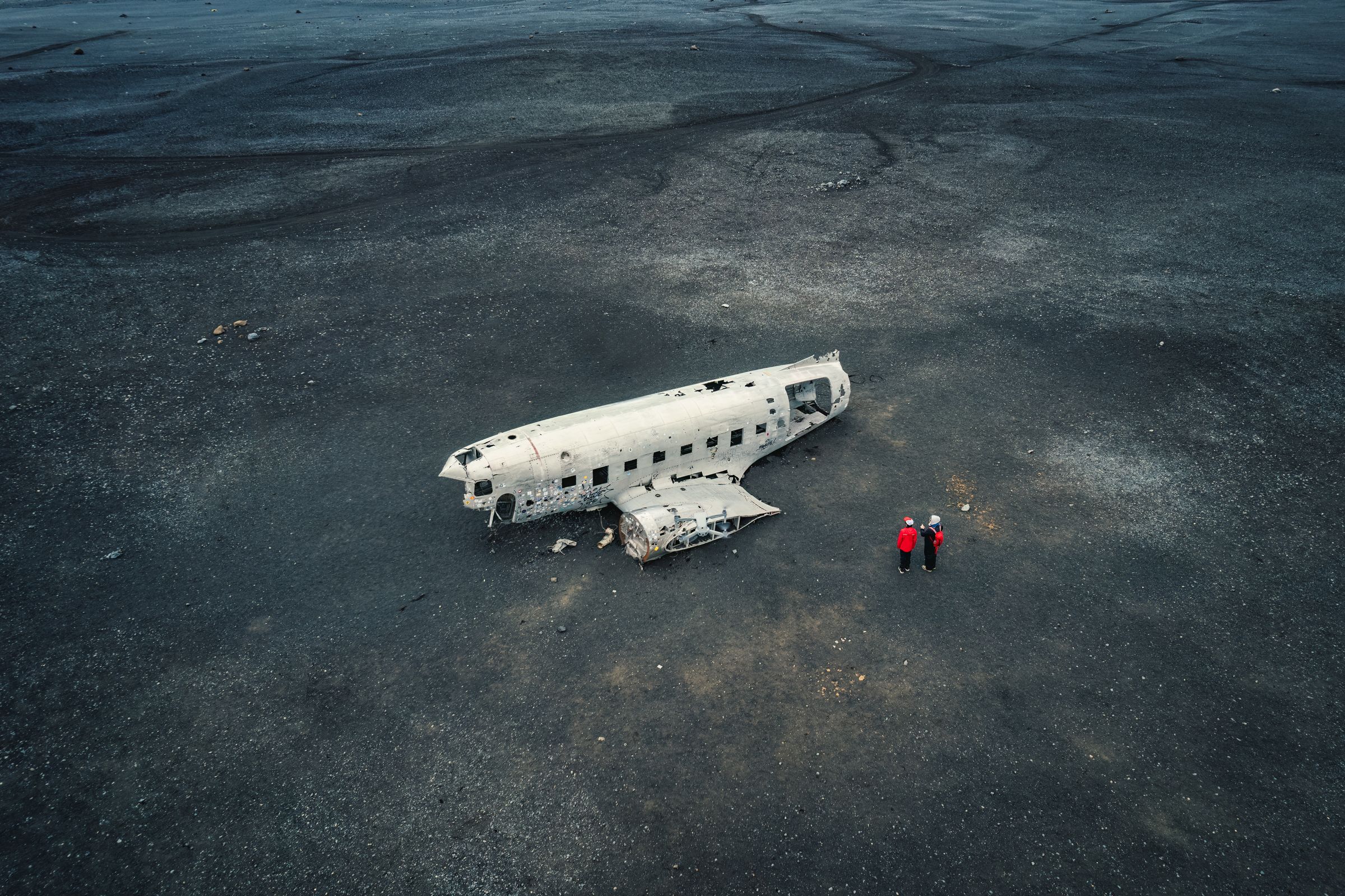 una vista aérea de dos personas de pie junto a un avión estrellado en medio de un desierto.