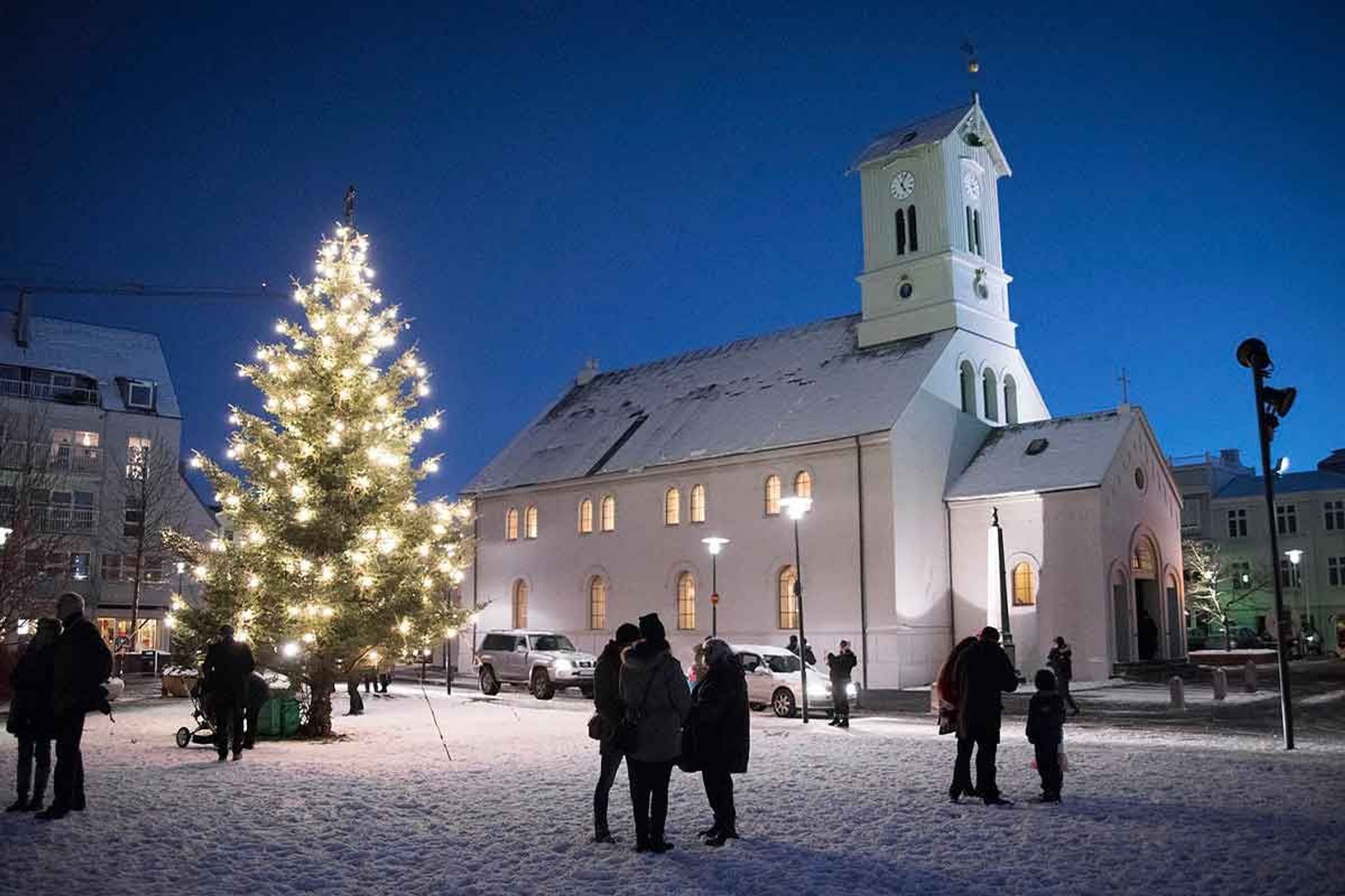 a christmas tree is lit up in front of a church in the snow .