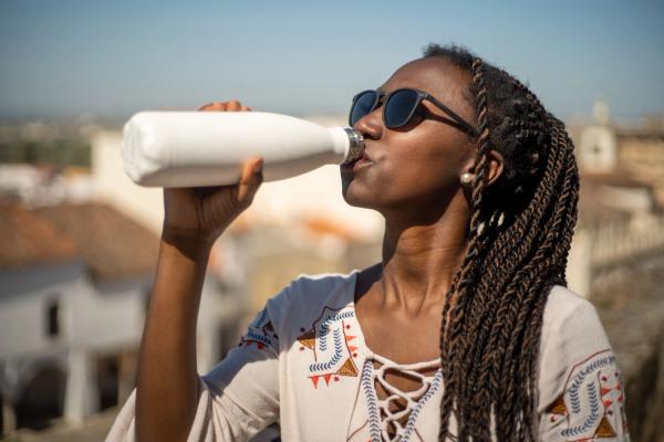 Black girl with braids and glasses drinking from a white reusable bottle