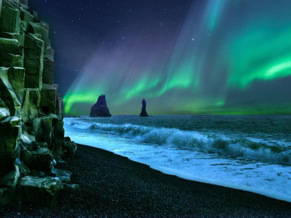 the aurora borealis is shining over the ocean at vík in south iceland.