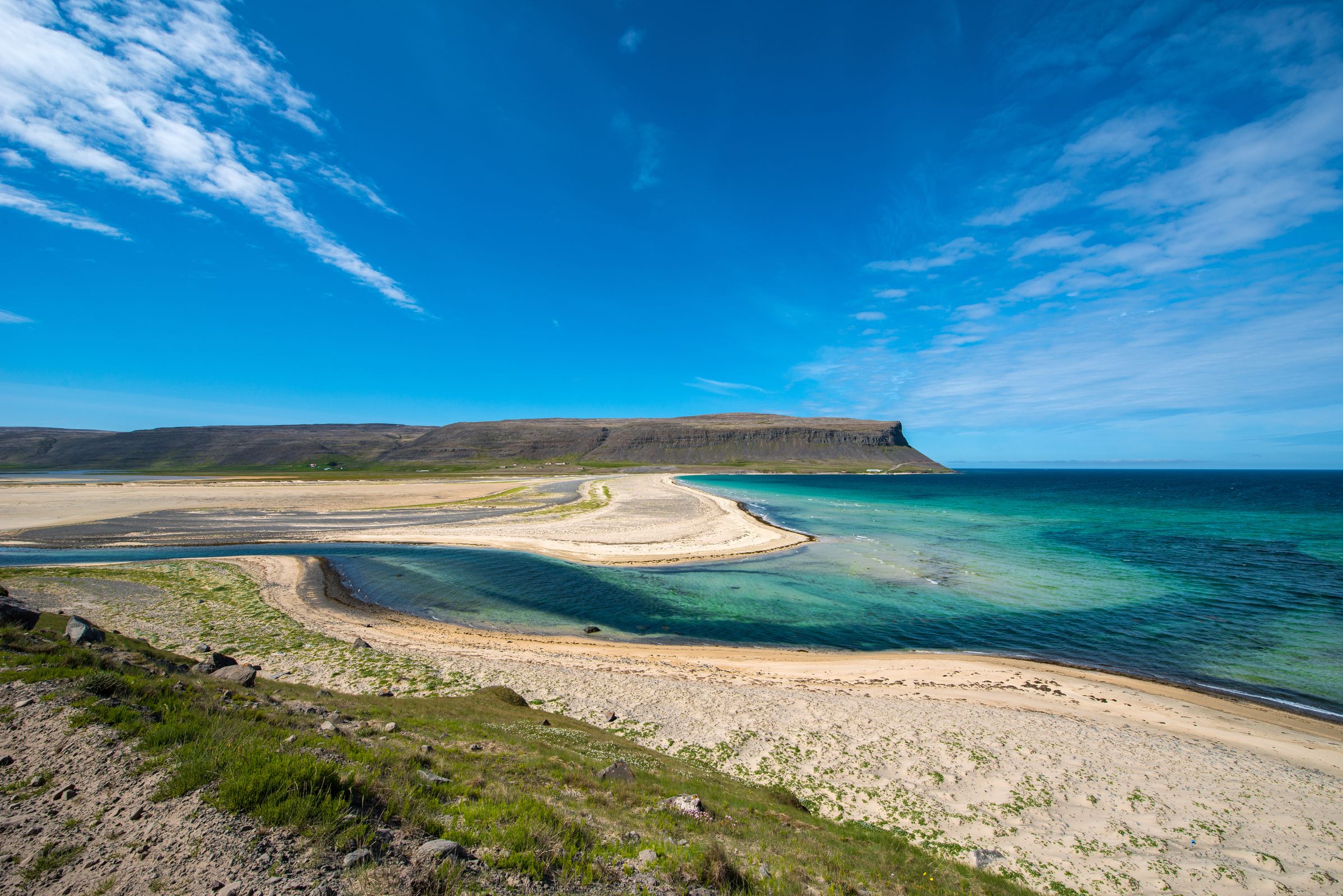 une plage avec une montagne en arrière-plan et une rivière qui la traverse.