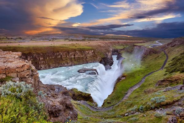 a waterfall in the middle of a valley with a sunset in the background .