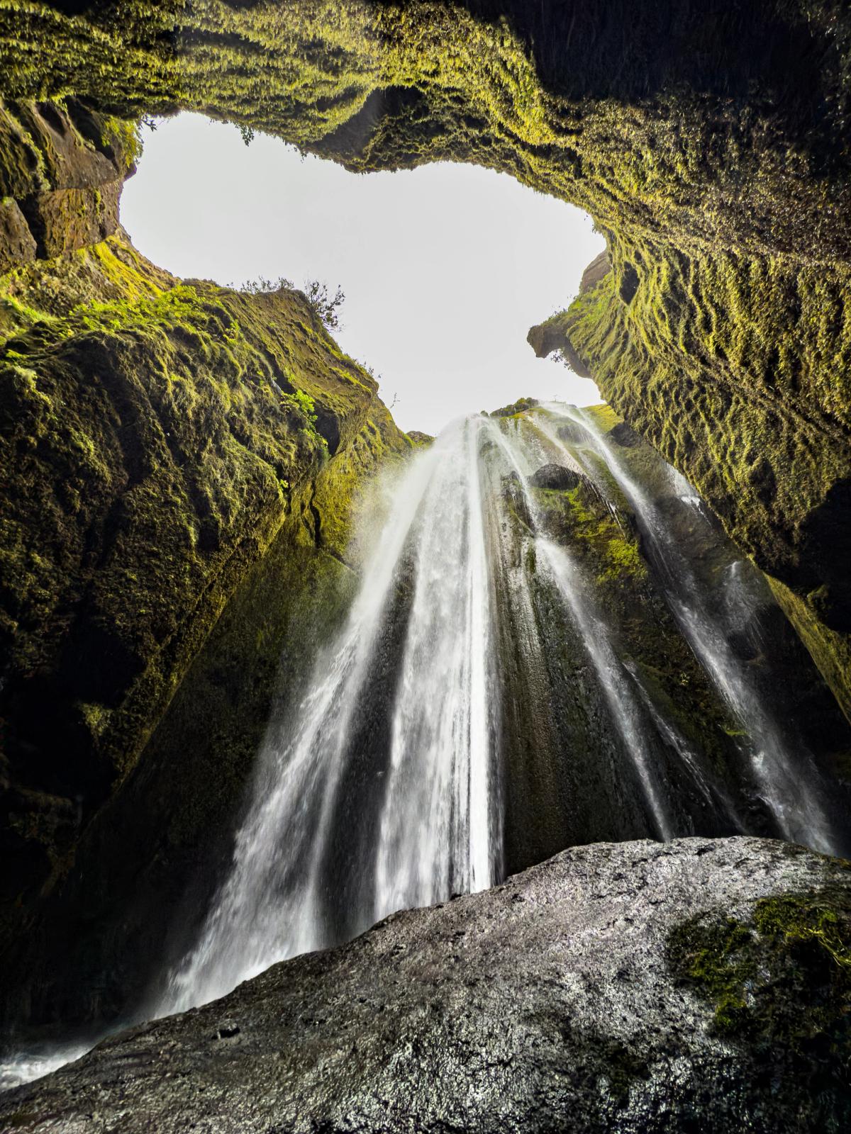 A waterfall cascades into a dark, moss-covered cave from an opening above.