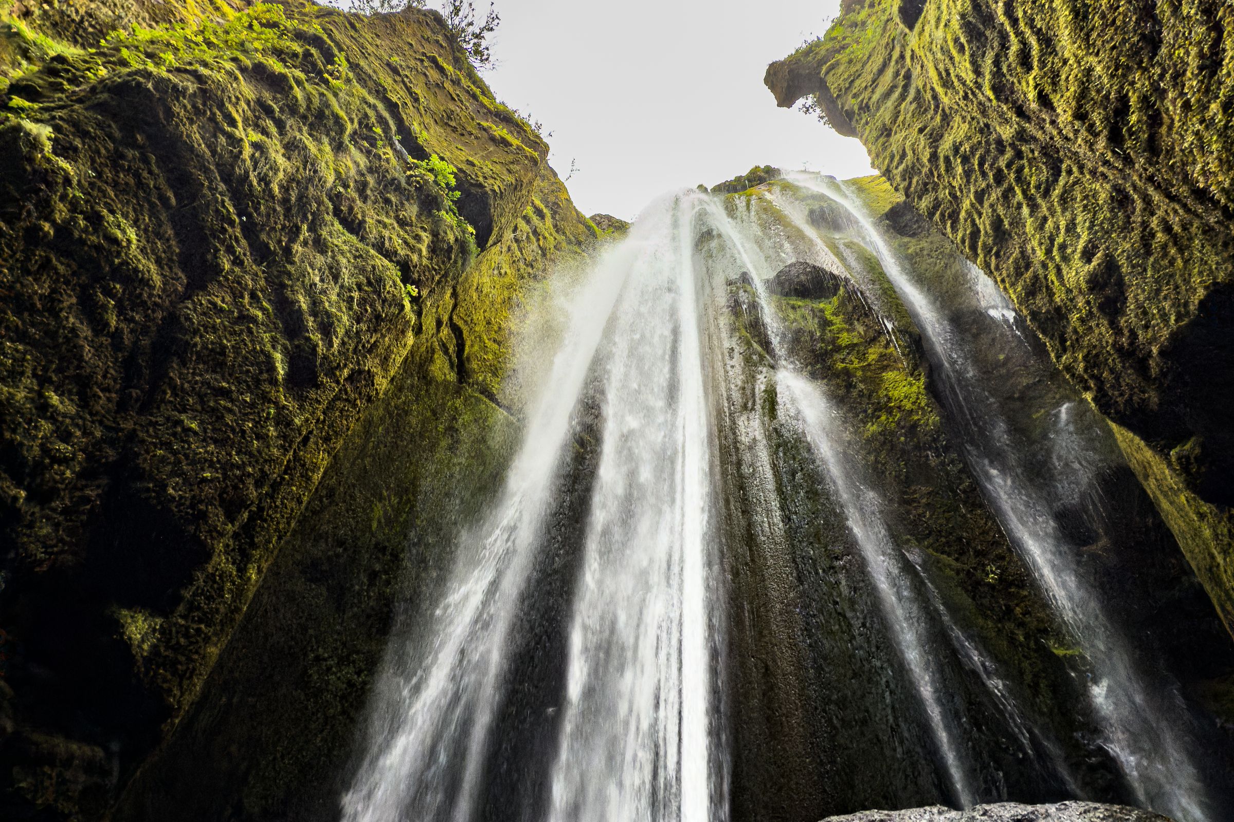 A waterfall cascades into a dark, moss-covered cave from an opening above.