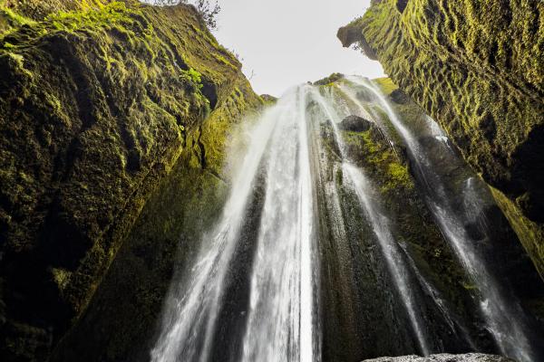 Una cascada cae en una cueva oscura cubierta de musgo desde una abertura en lo alto.