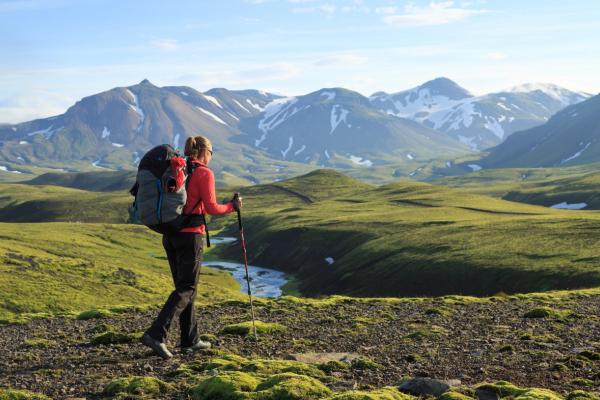 a woman with a backpack is hiking in the mountains wearing hiking pants in iceland.