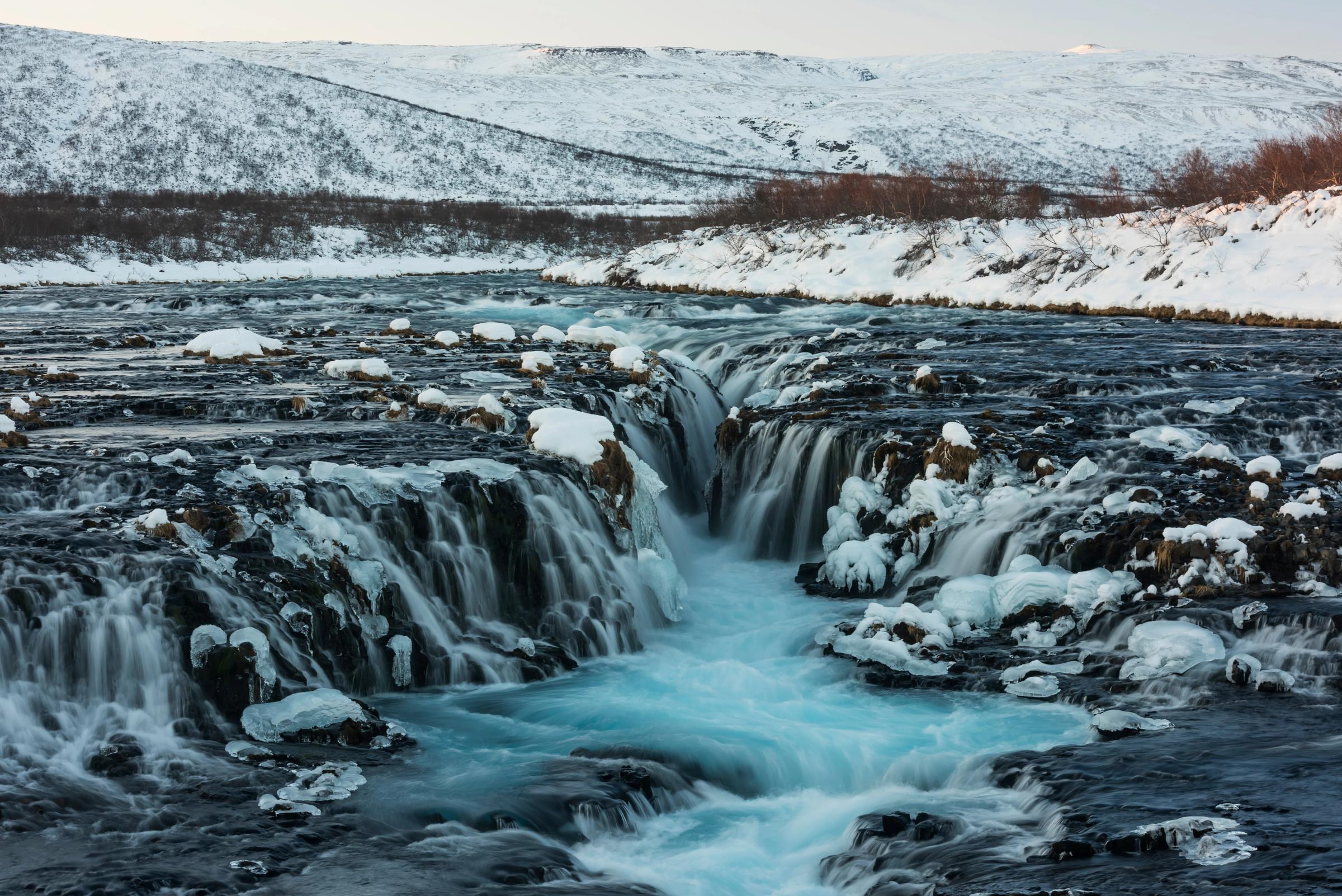 una cascada está rodeada de nieve y hielo en medio de un río.