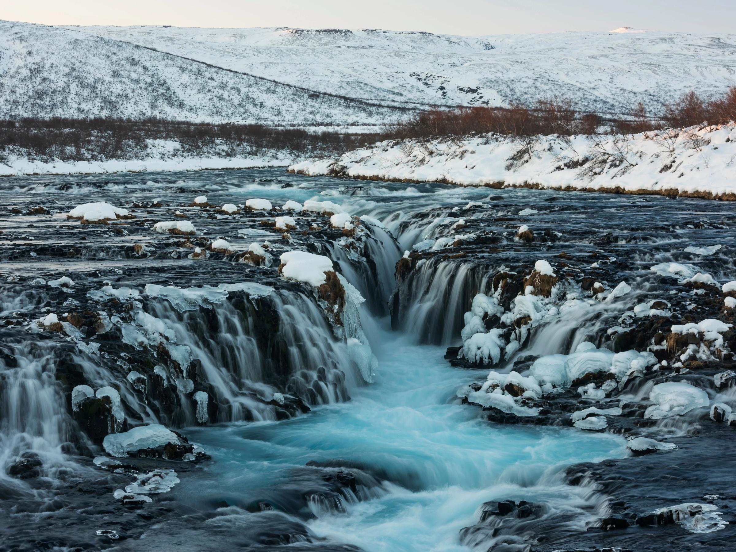 una cascada está rodeada de nieve y hielo en medio de un río.