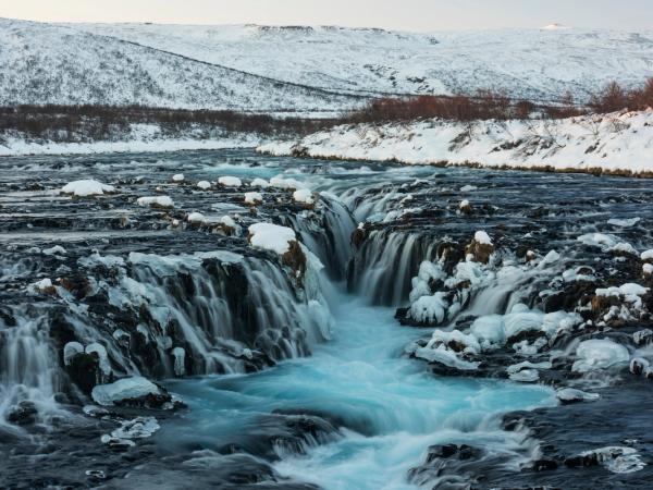 a waterfall is surrounded by snow and ice in the middle of a river .