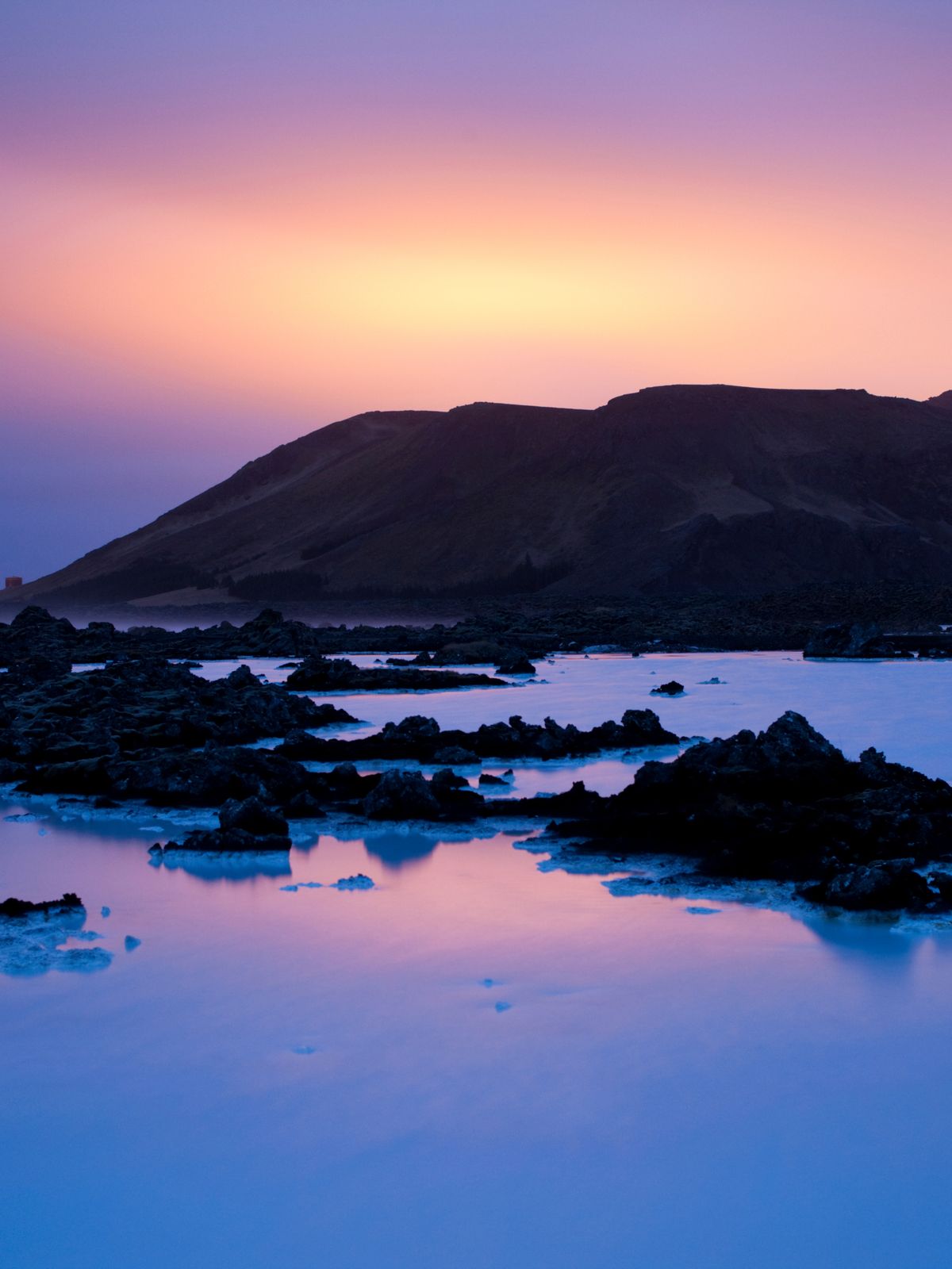 una puesta de sol sobre un lago con rocas y montañas al fondo.