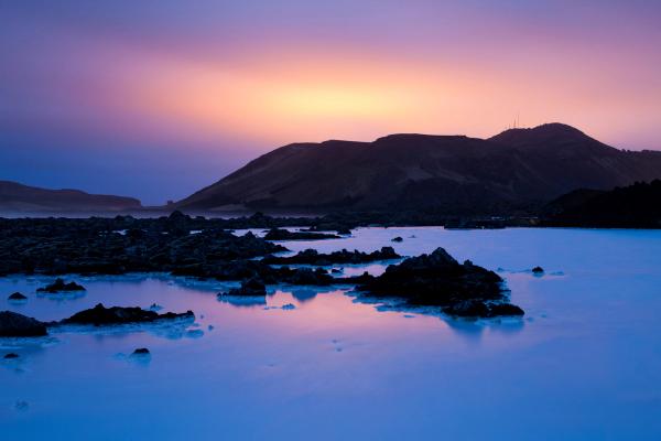 a sunset over a lake with rocks and mountains in the background .