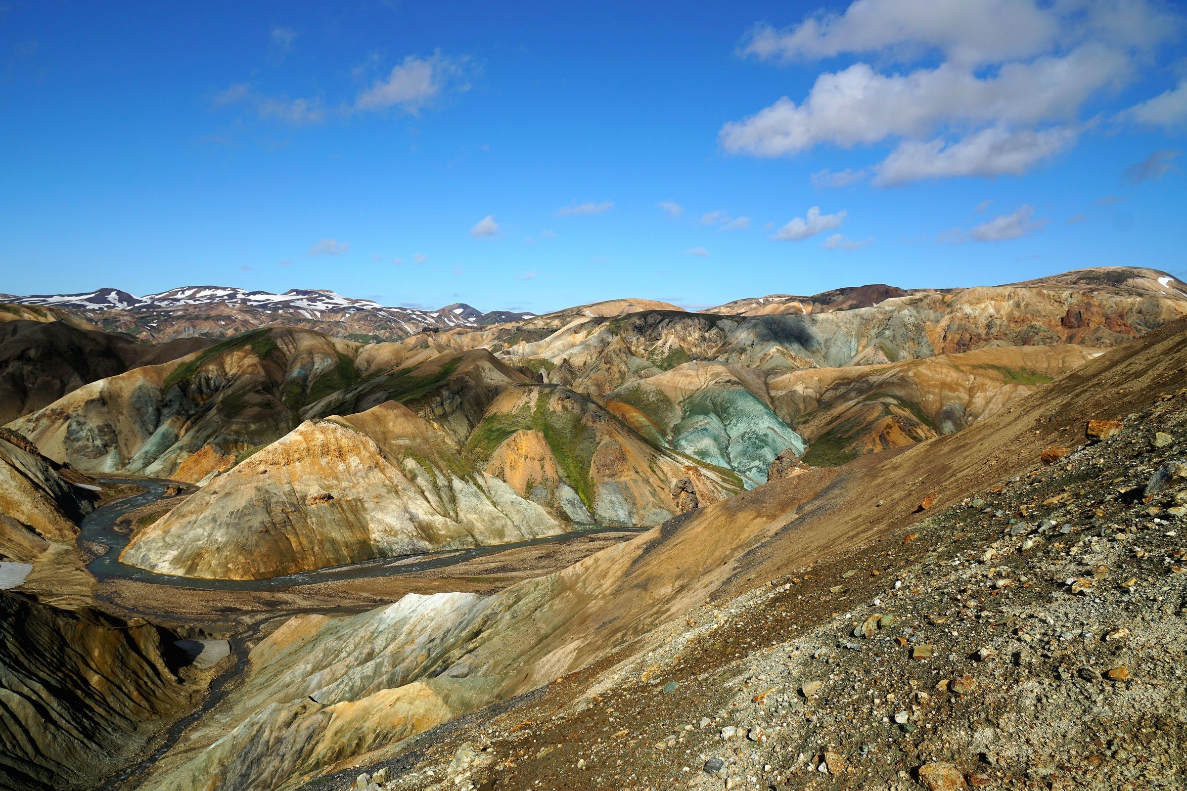 a river runs through a valley surrounded by mountains on a sunny day .