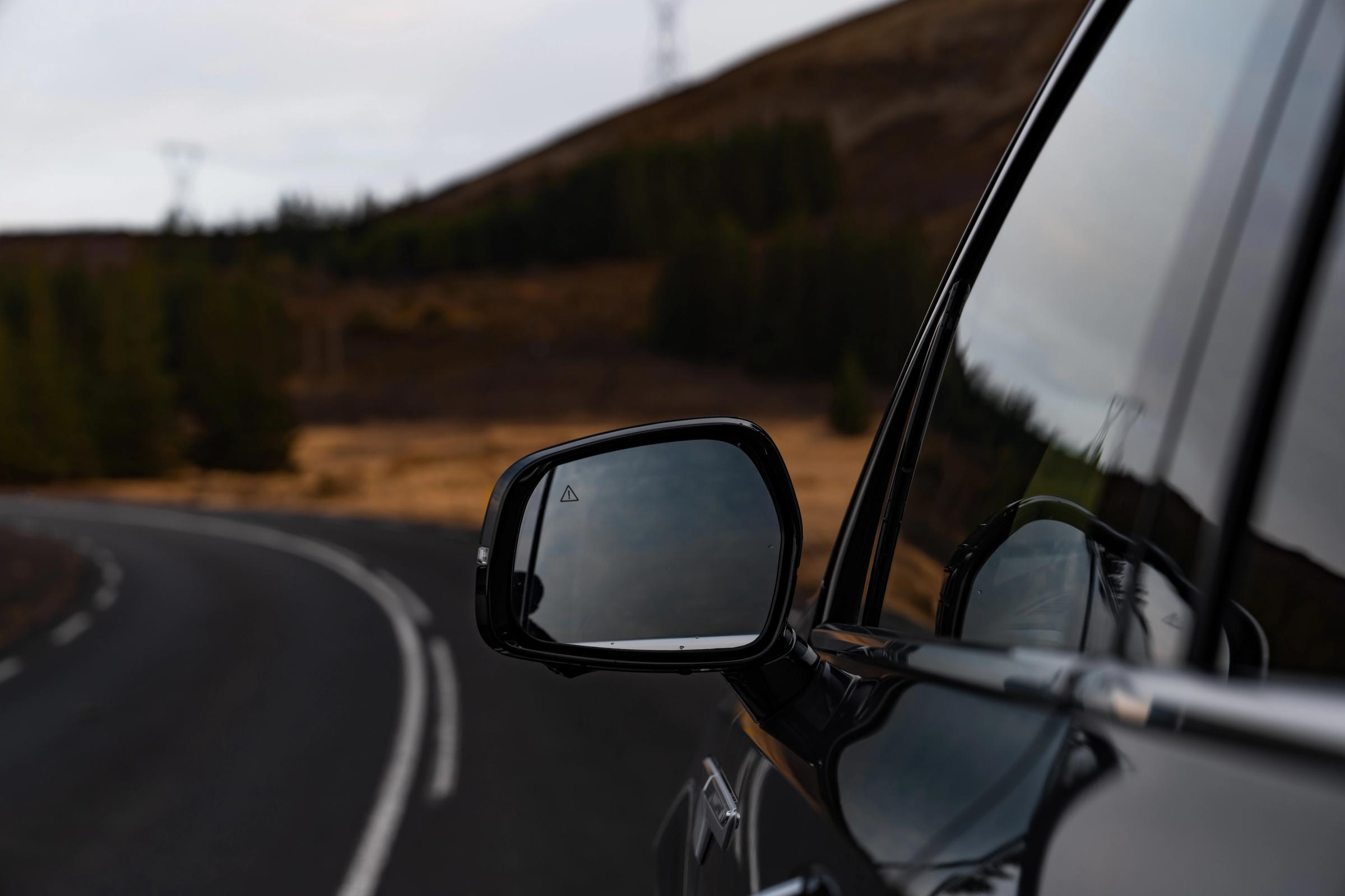 Gros plan sur le rétroviseur extérieur d’un Kia Sorento, avec une route de montagne qui s’y reflète