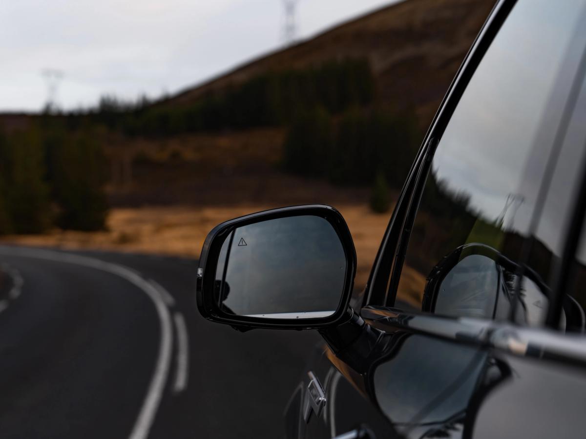 Rétroviseur extérieur pour Sorento Gros plan sur le rétroviseur extérieur d’un Kia Sorento, avec une route de montagne qui s’y reflète