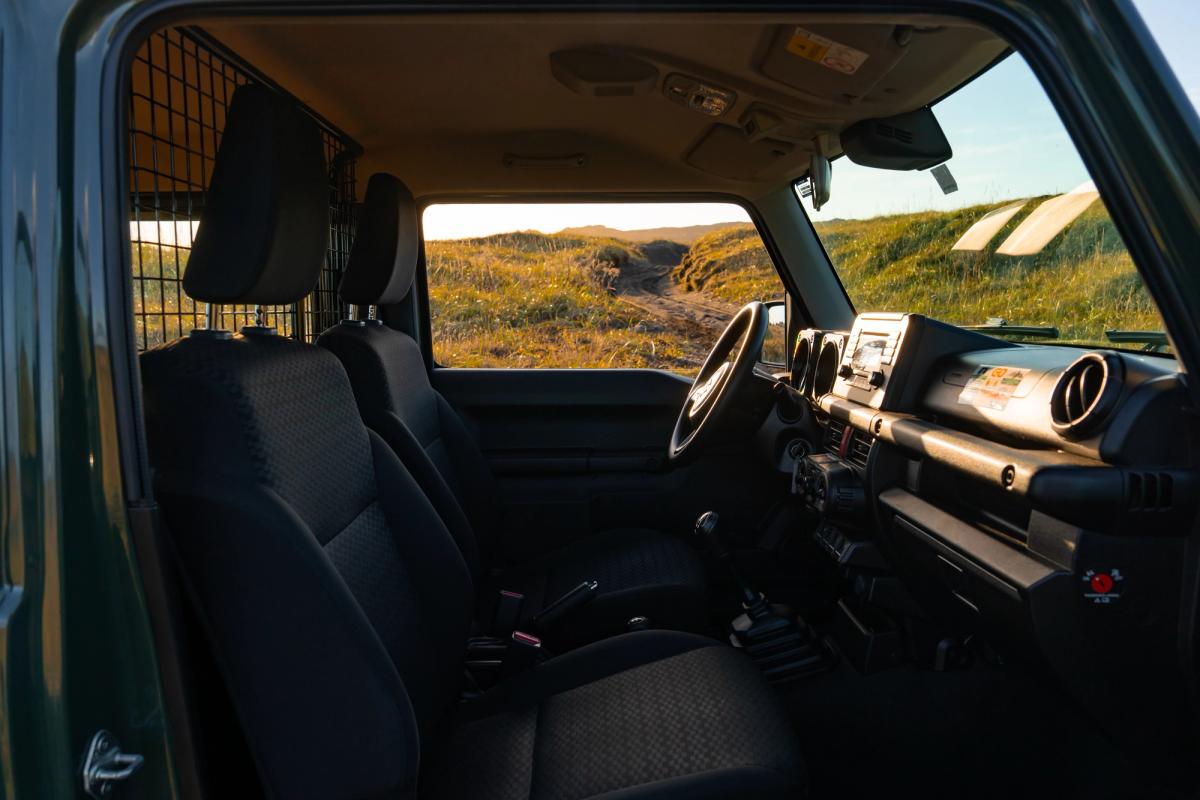 Innenraum eines Suzuki Jimny mit Schaltgetriebe, durch die Beifahrertür fotografiert, mit Armaturenbrett und Sitzen