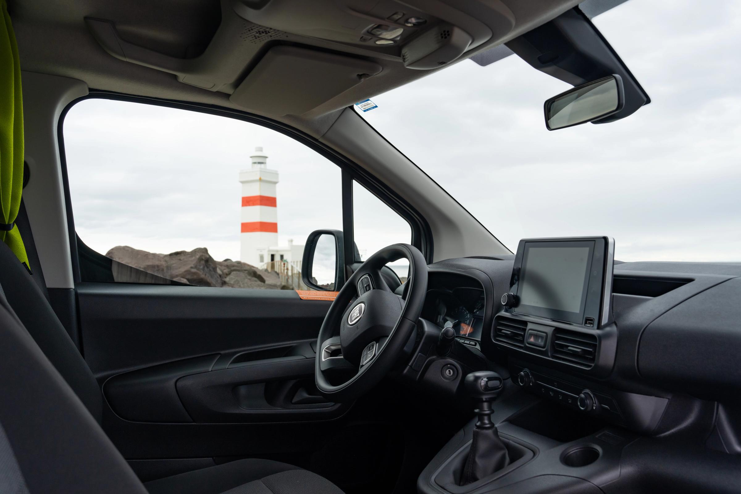 Cabina del conductor con volante, pantalla táctil y palanca de cambios manual; se ve un faro por la ventanilla lateral