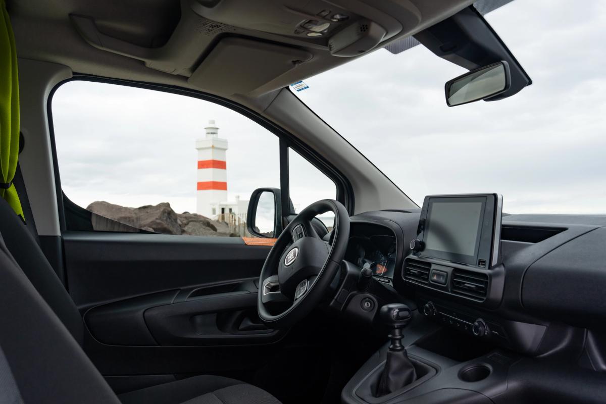 Cabina del conductor con volante, pantalla táctil y palanca de cambios manual; se ve un faro por la ventanilla lateral