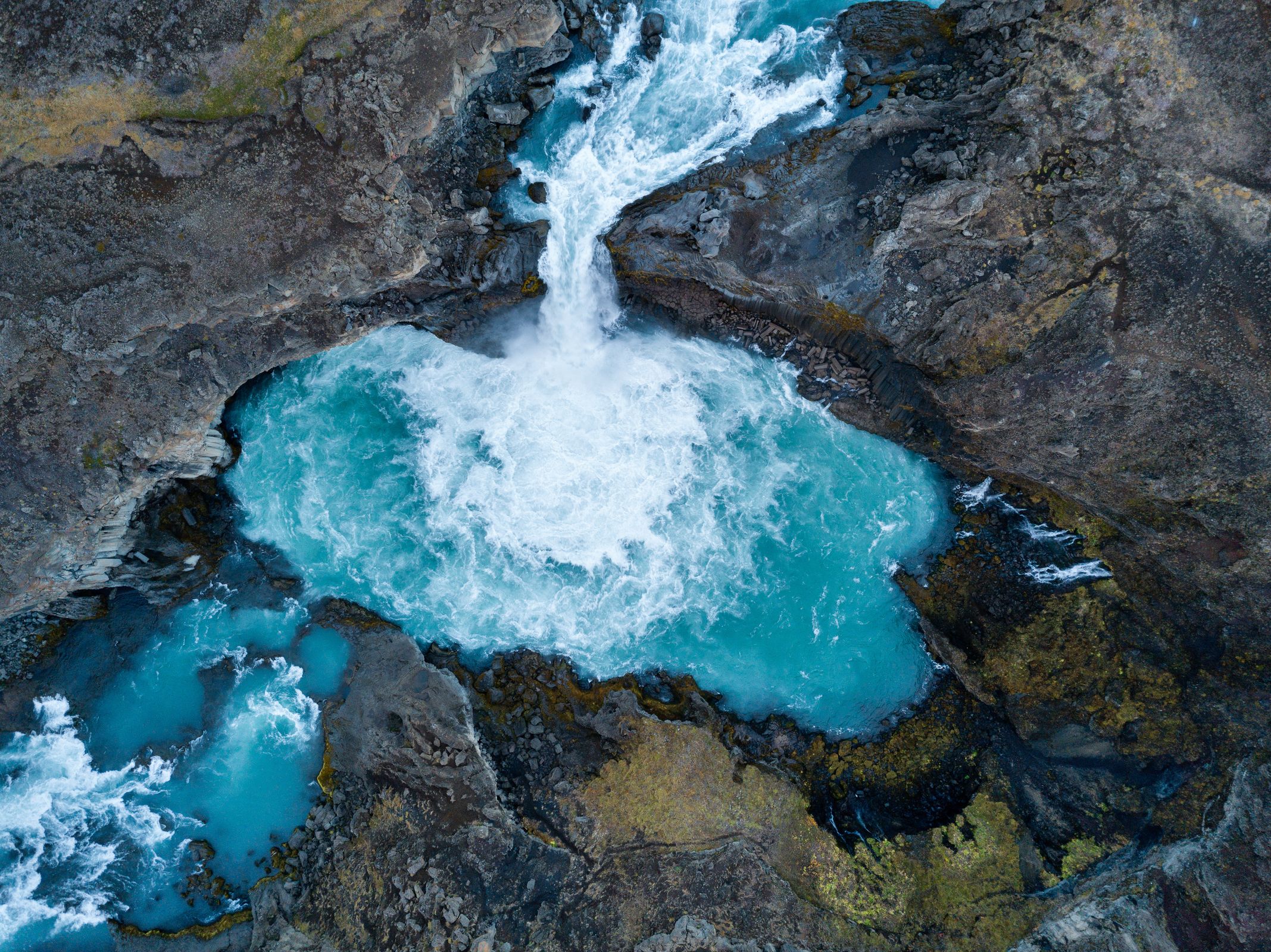 Aerial view of a turquoise waterfall cascading into a rocky pool.