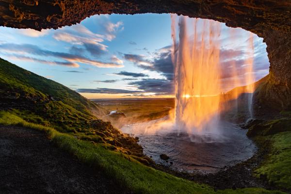 a waterfall is coming out of a cave at sunset in iceland.