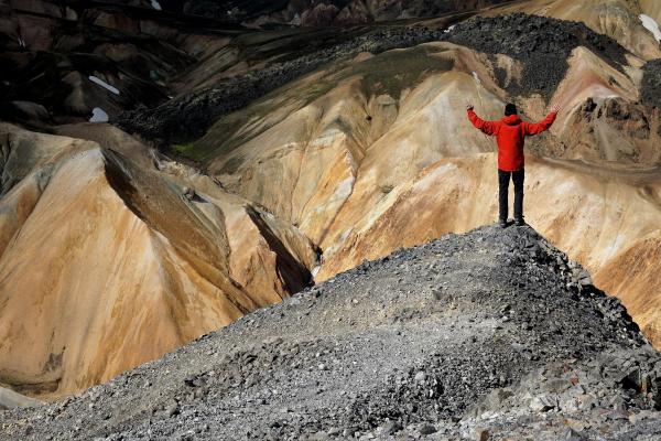 a man in a red jacket is standing on top of a rocky mountain .