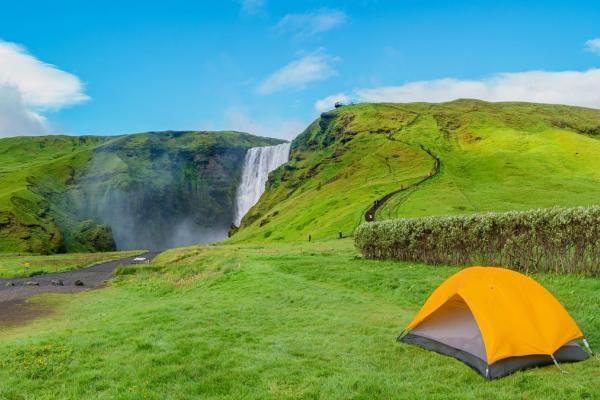 Skógar Campsite in Iceland Panoramic view over camping site with orange tent, and tourists in front of famous Skogafoss waterfall, while hiking in Iceland, summer, scenic view.