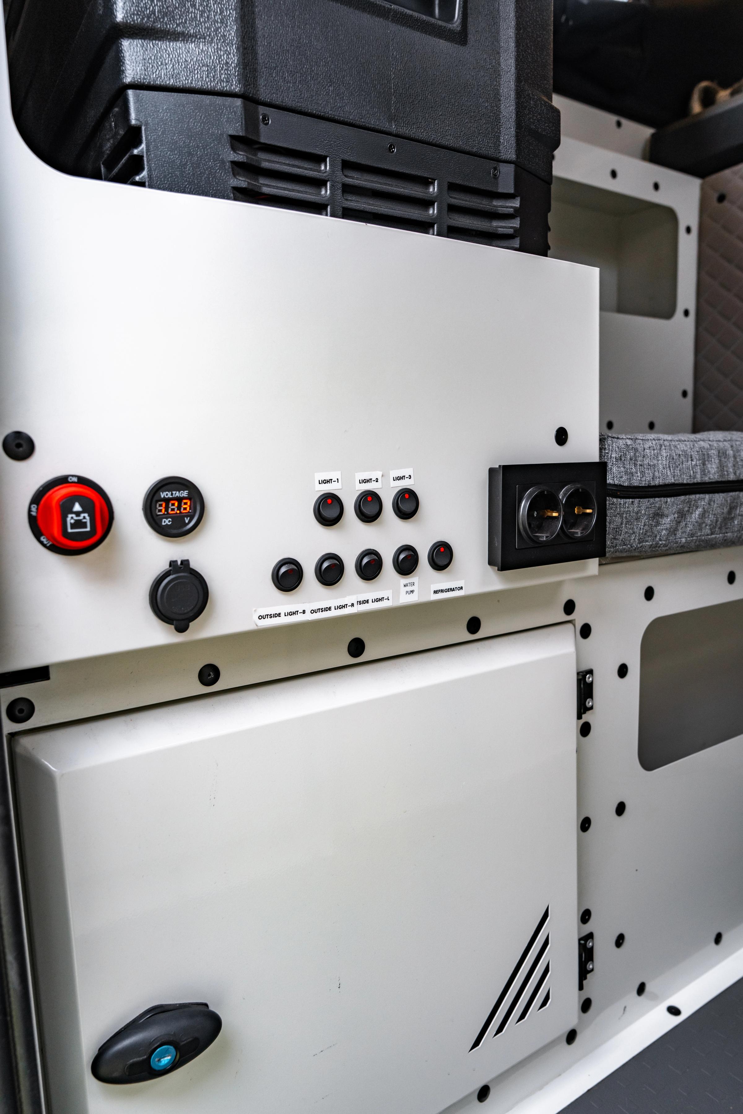 Panel con interruptor de batería, indicador de voltaje, toma de 12 V y enchufes debajo de la nevera portátil