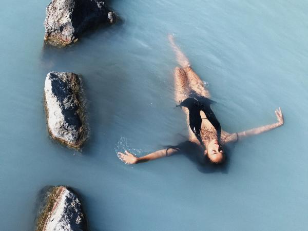 Woman floating peacefully in the milky blue geothermal waters of Sky Lagoon, surrounded by dark volcanic rocks.