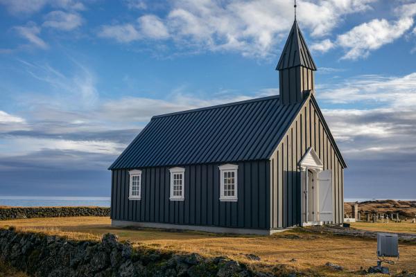a small black church with a steeple in the middle of a field .