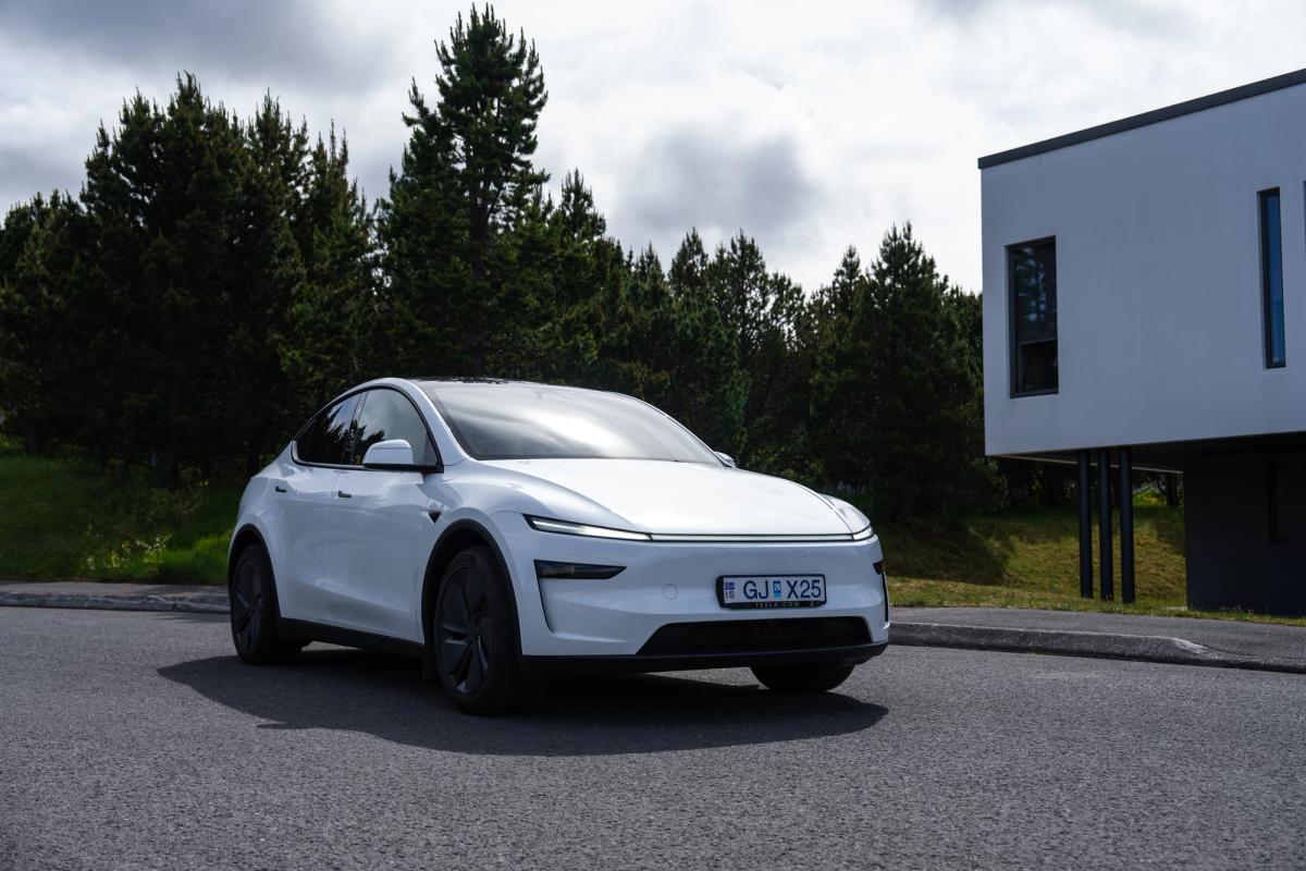 Coche eléctrico Tesla Model Y aparcado cerca de unos pinos y un edificio moderno en Islandia