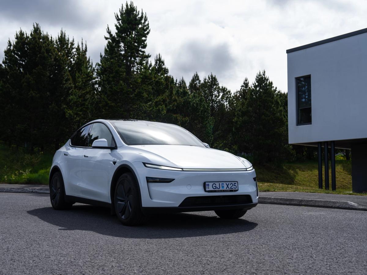 Aparcado junto a un edificio moderno Coche eléctrico Tesla Model Y aparcado cerca de unos pinos y un edificio moderno en Islandia